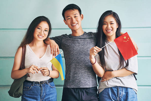 Group of three happy international chinese asian students smiling and holding flags of China and Ukraine in university Group of three international chinese asian students smiling and holding flags of China and Ukraine in university expatriate photos stock pictures, royalty-free photos & images