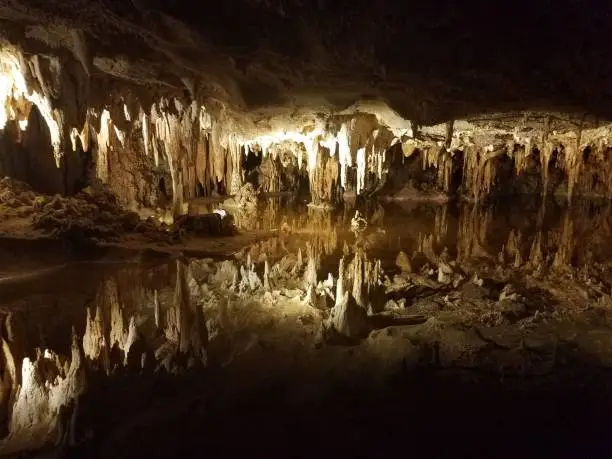 brown stalactites and stalagmites in a cave or cavern with water and reflection