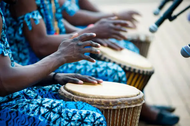 hands of African drummers in blue costumes and traditional drums in front of microphones at a performance