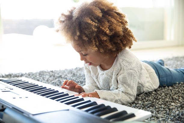 ethnic curly girl playing piano on carpet - practicing piano child playing imagens e fotografias de stock