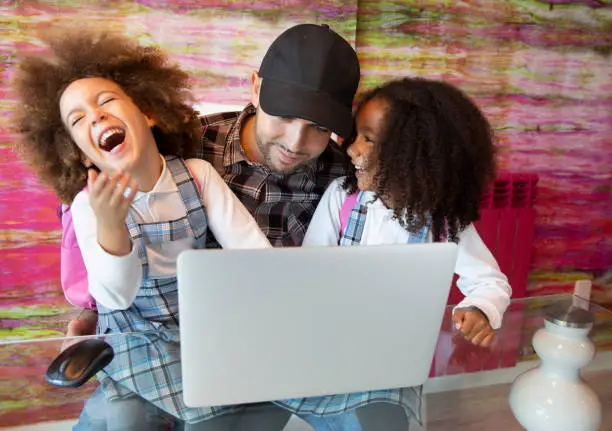 Ethnic sister kid girls playing laptop with father having fun laughing