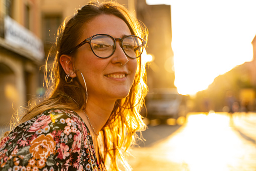Young woman at the street at sunset. She is wearing a flowers print dress and eyeglasses.