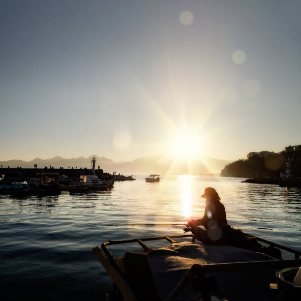 Silhouetted people relaxing in Antalya harbor over sunset sky and high mountains
