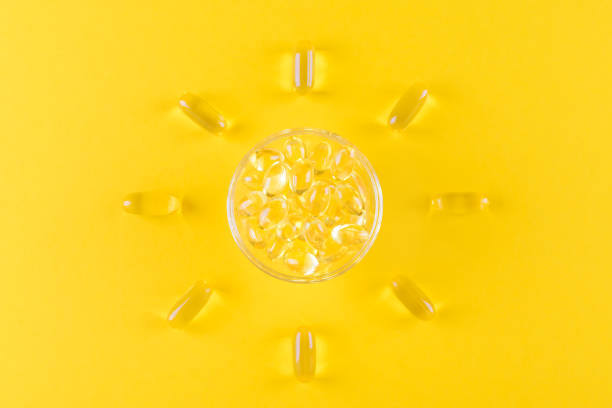 cápsulas de omega de oro como el sol sobre fondo amarillo, plana sensila - vitamin d fotografías e imágenes de stock