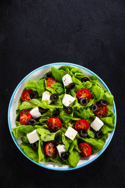 Greek salad on black stone plate Feta cheese with sliced tomatoes , lettuce, cucumber, black olives and onion side salad stock pictures, royalty-free photos & images