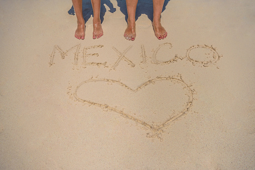 Legs on the background of the inscription on the sand Mexico.