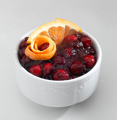 Full white bowl with fresh red cranberries on dark brown wooden table background. Eating healthy berries. Closeup. Top down view.