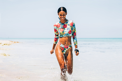 Millennial Black woman running on tropical sandy beach. She is enjoying her  summer vacation in Caribbean.