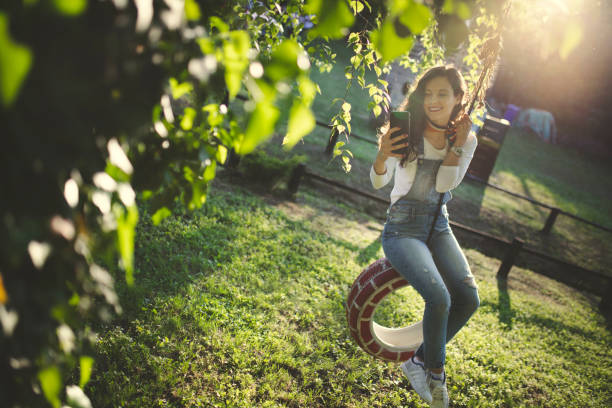 donna che usa il telefono sull'altalena degli pneumatici - freedom tire swing tire swing foto e immagini stock