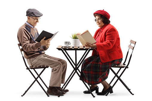 Full length shot of an elderly man and woman at a cafe reading books isolated on white background