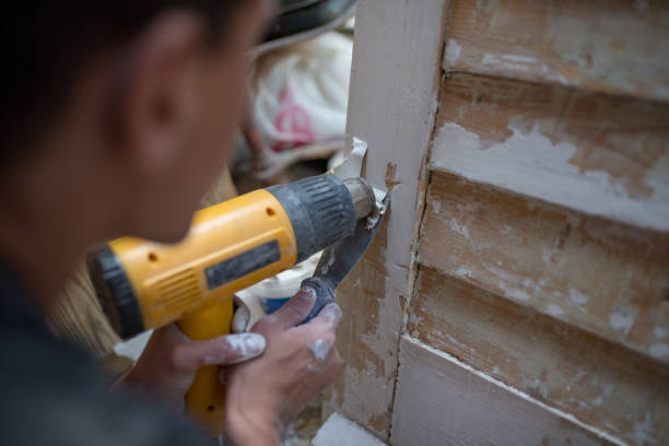 Handyman using hot-air gun to remove old paint, scrubbing  old paint from  wood surface.