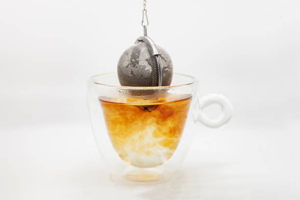 Tea strainer with tea leaves dropped in glass cup of boiling water Tea strainer infused in glass cup with boiling water, closeup on a white background glass cup of boiling water stock pictures, royalty-free photos & images
