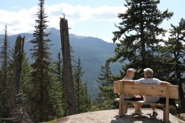 istock Couple sit on bench amongst mountains and forest 1173436878