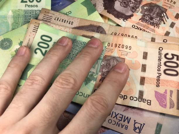 istock Many mexican pesos bills spread randomly over a flat surface with a hand over them 1173437273