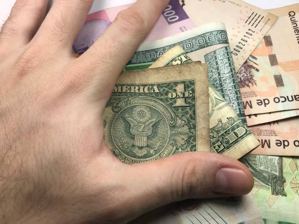 istock Many mexican pesos bills spread randomly over a flat surface with a hand over them 1173443547
