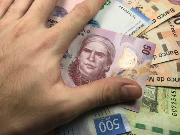 istock Many mexican pesos bills spread randomly over a flat surface with a hand over them 1173443795