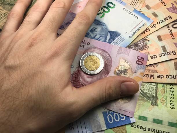 istock Many mexican pesos bills spread randomly over a flat surface with a hand over them 1173443878