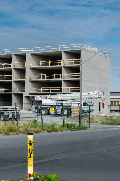 istock Partially constructed concrete four storey building under a blue sky with a mobile crane, construction fence and roadway in the foreground 1173447341