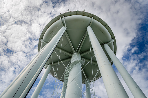Underside landscape view of a water tower against a cloud filled sky showing winding spiral stairs on the outside of the center column.