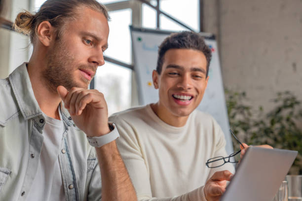 feche acima do tiro de dois homens modernos novos no desgaste ocasional esperto que trabalha junto ao sentar-se no escritório - mid adult men smart casual white happiness - fotografias e filmes do acervo