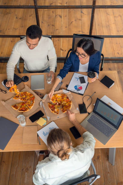 vista superior de los empresarios en ropa casual sentado en la mesa y comer pizza para el almuerzo - lunch business office business lunch fotografías e imágenes de stock