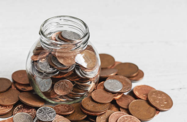istock Full jar of coins on a table, surrounded by loose change. 1173455488