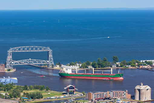 A ship passing under a lift bridge into harbor.