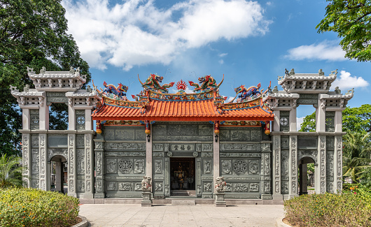 Manila, Philippines - March 5, 2019: Chinese Cemetery in Santa Cruz part of town. Gray stone ceremonial hall and temple with extensively colorfully decorated red roof under blue sky. Green foliage.