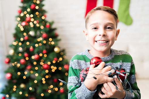 Cheerful boy holding Christmas decorations at home during festive preparations