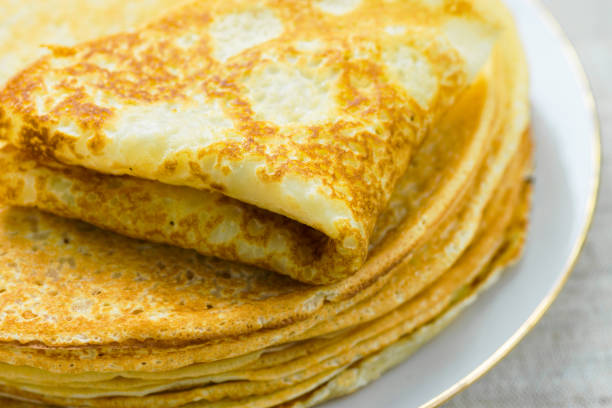 istock Stack of folded delicious freshly baked crepes with appetizing golden crust on white plate on linen table cloth by window in sunlight. Cozy atmosphere breakfast morning 1173476432