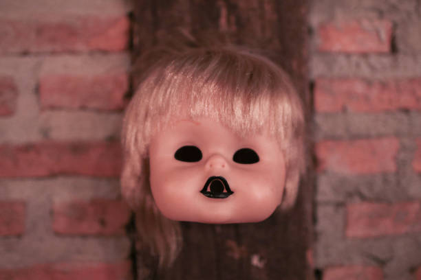 face e cabeça quebradas da boneca que penduram na decoração da parede de tijolo para o partido de halloween - doll evil child baby - fotografias e filmes do acervo