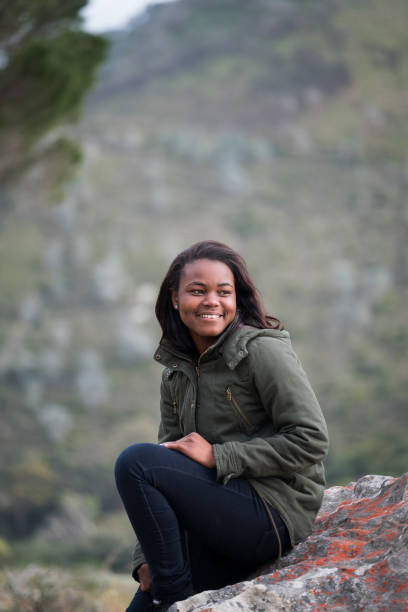 istock Smiling African woman looking away while sitting on rock 1173481419