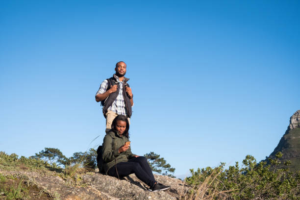 istock Man standing by girlfriend sitting on cliff 1173482875