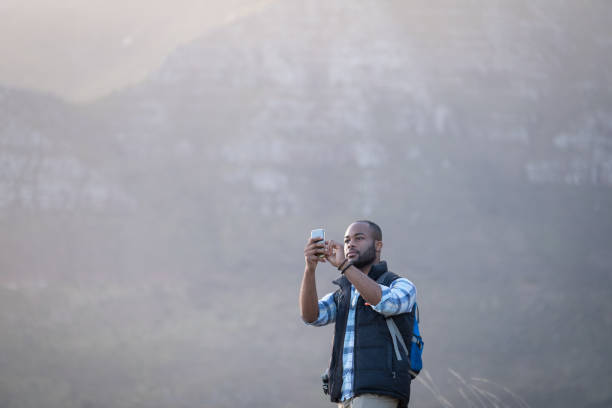 istock Man standing on cliff against rocky mountains taking a photograph 1173482886