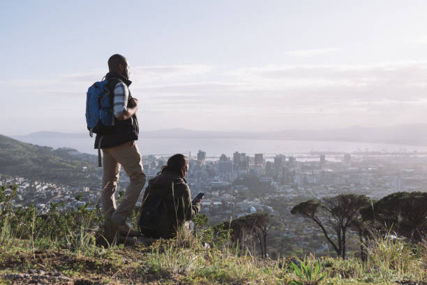 Man standing by woman sitting on cliff against sky