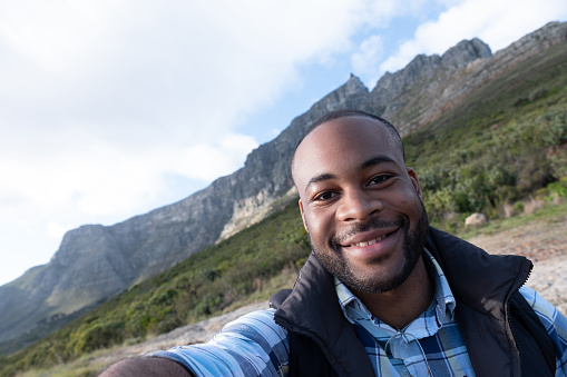 Close-up portrait of smiling man on Table Mountain. Male hiker is happy during vacation. He is wearing jacket against sky.
