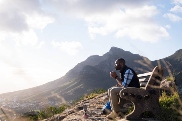 nachdenklicher mann, der trinkt, während er auf der bank sitzt - tafelberg berg stock-fotos und bilder