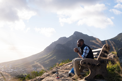 Side view of thoughtful man sitting on bench. Male hiker having drink while looking at view. He is on vacation at Table Mountain.