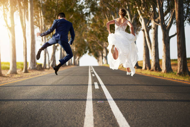 Happy endings aren't just for fairytales Rearview shot of a young couple jumping for joy on a country road on their wedding day free wedding stock pictures, royalty-free photos & images