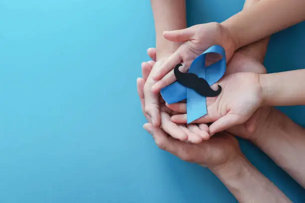 Family hands holding light blue ribbonwith mustache on blue background , Prostate Cancer Awareness, Men health awareness