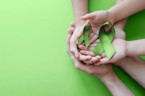 manos adultas y niños sosteniendo lime green ribbon sobre fondo verde, concienciación sobre la salud mental y concienciación sobre el linfoma, día mundial de la salud mental - kidney cancer fotografías e imágenes de stock