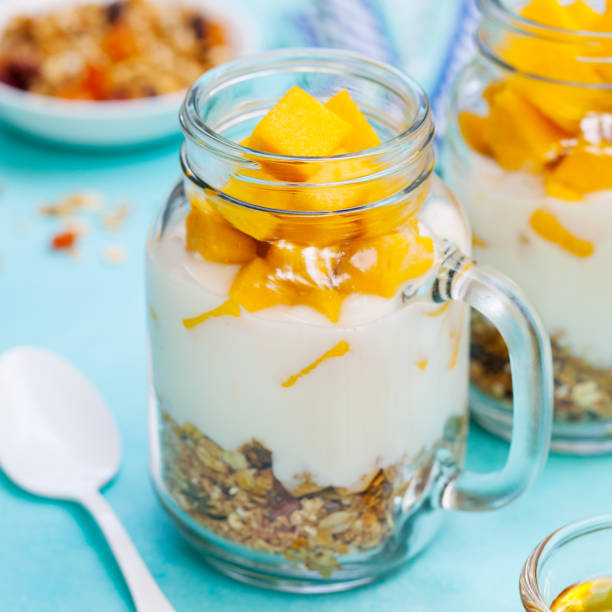 istock Healthy breakfast, dessert. Fresh mango fruit with yogurt and granola in jars. Blue background. 1173501817
