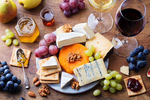 Assortment of cheese, grapes with red and white wine in glasses. Wooden background. Top view.