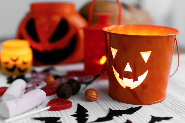 istock Halloween jack o lantern bucket, glowing candle, festive candy, skulls, black bats, ghost, spider decorations on white wooden background. Copy space. Trick or treat 1173505290