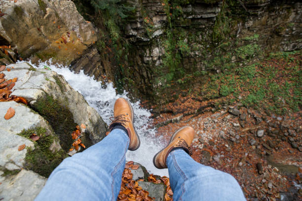 istock man legs in blue jeans and brown boots sitting on the edge looking at waterfall 1173506510