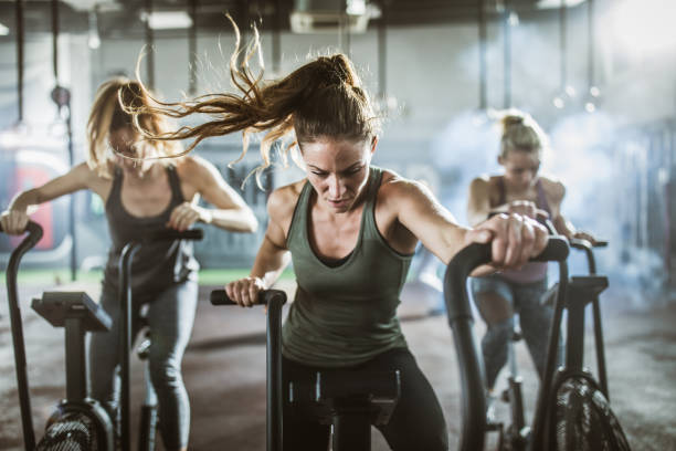 Group of athletic women on exercise bikes in a health club. Young athletic women exercising on bikes during cross training in a health club. Focus is on woman in the foreground. spin bike stock pictures, royalty-free photos & images
