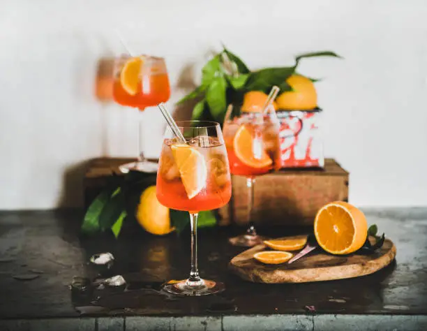 Spritz aperitif alcohol cold drink in glasses with fresh oranges and ice cubes on concrete table, white wall at background. Summer refreshing drink concept