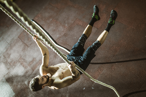 High angle view of determined man exercising endurance while holding himself for two ropes in a health club. Copy space.