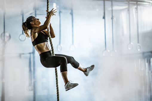 Female athlete moving up the rope during cross training in a health club. Copy space.