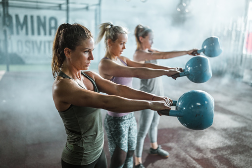 Group of young athletic women exercising with kettle bells in a gym. Focus is on woman in the foreground.